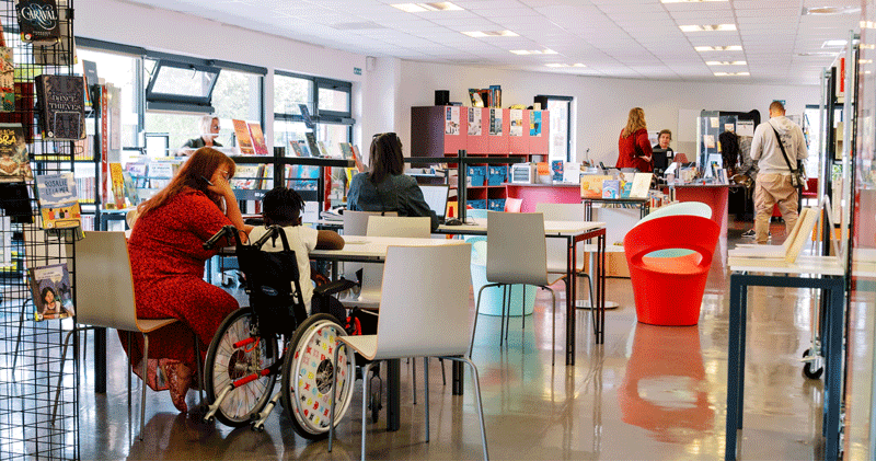 Femme et enfants en chaise roulante assis dans l'espace de lecture d'une mediathèque