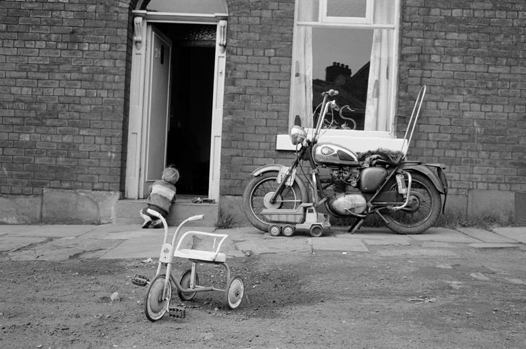 Photographie en noir et blanc d'un moto et d(u tricycle garés devant une maison