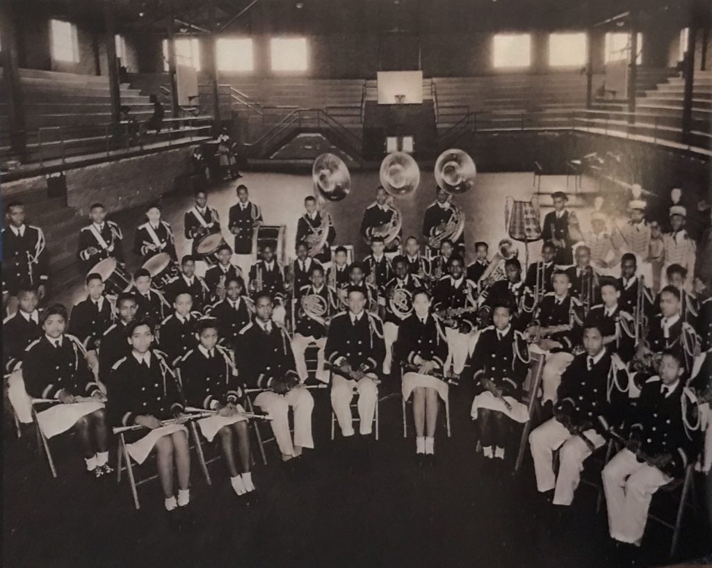Photo en noir et blanc d'une fanfare avec les musiciens assis dans une salle